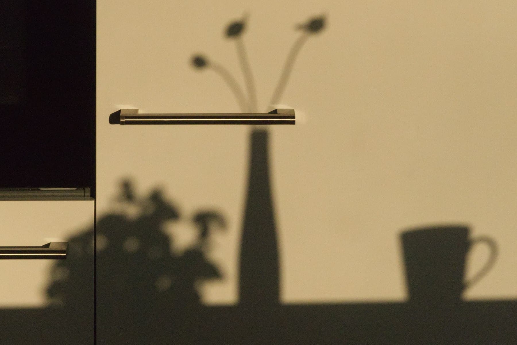 Sombras de un florero y una taza sobre una pared color arena